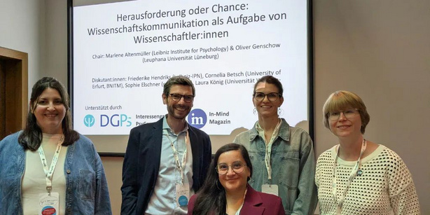Eine Gruppe von Wissenschaftler:innen steht vor einer Power Point Präsentation mit dem Titel : Herausforderung oder Chance: Wissenschaftskommunikation als Aufgabe von Wissenschaftler:innen